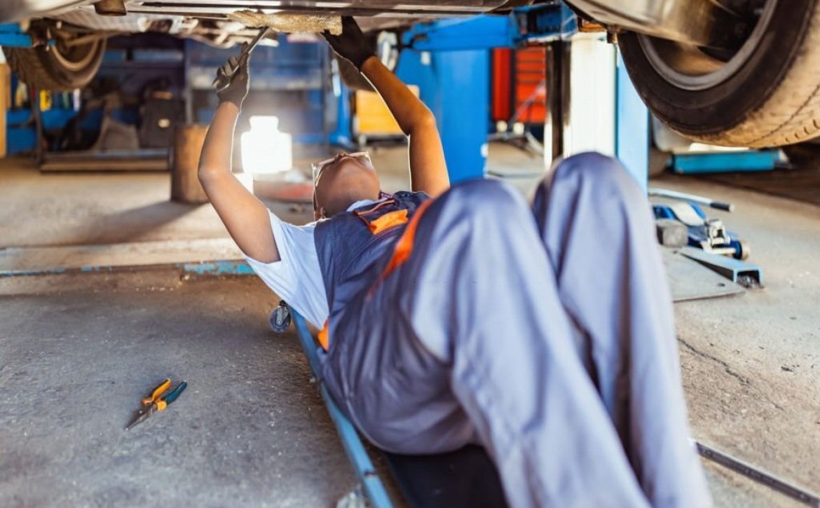 Mechanic lying down and working under the car in store. Side view.