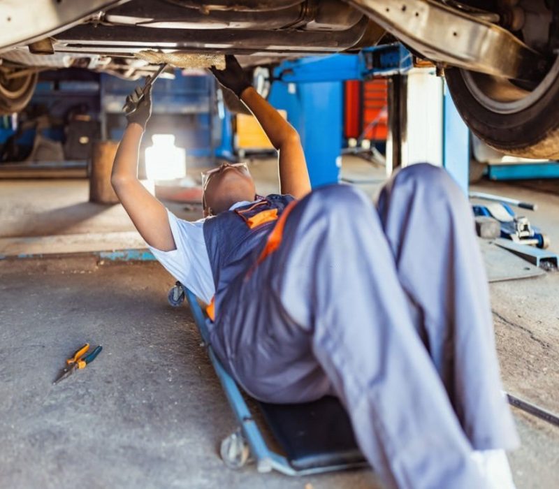Mechanic lying down and working under the car in store. Side view.
