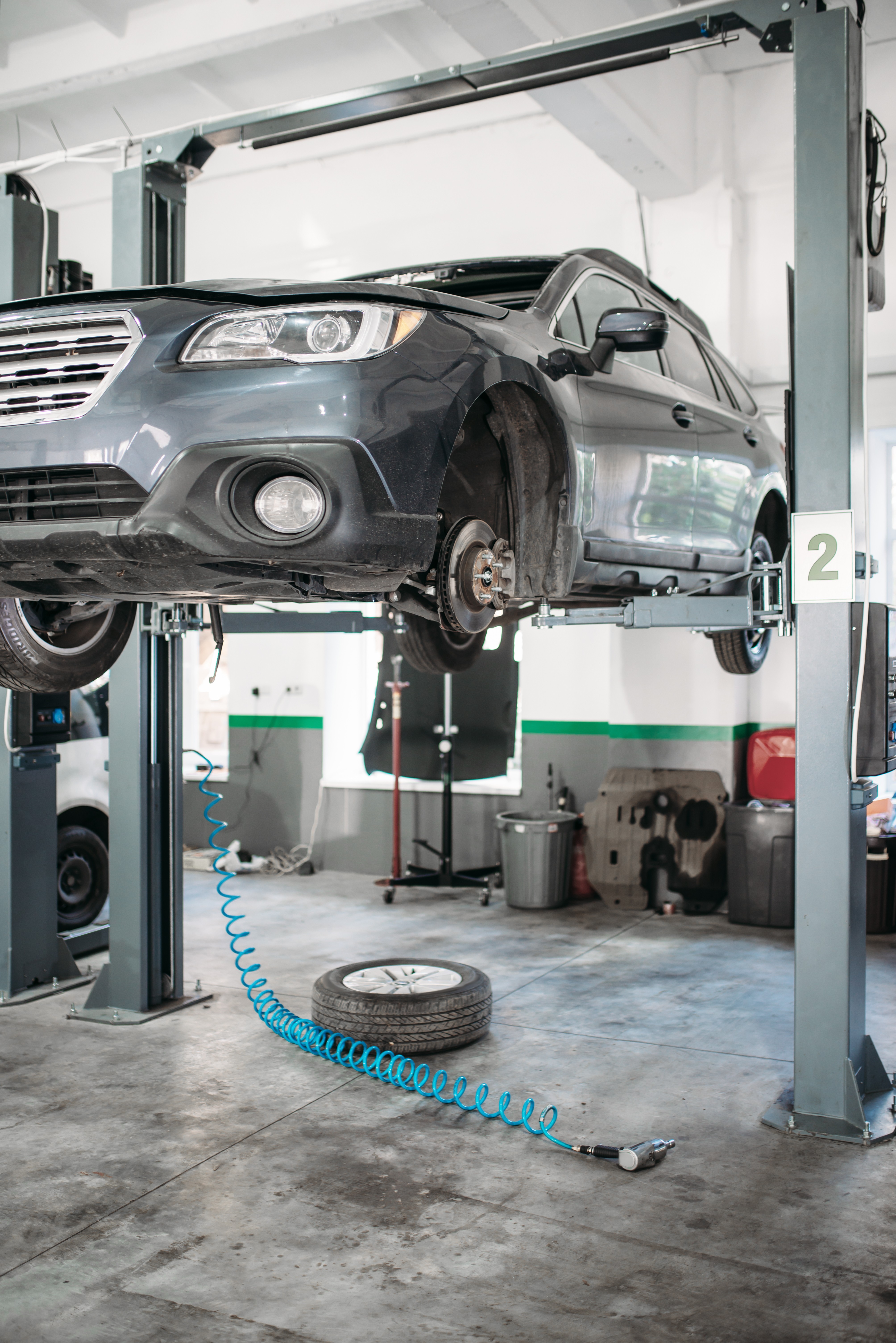 Car with removed wheel on the lift, nobody. Automobile repair, vehicle maintenance, tire service