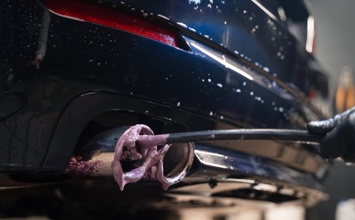 Detailing worker cleans exhaust pipe of car. Cleaning auto muffler with foam and brush. Detail car wash