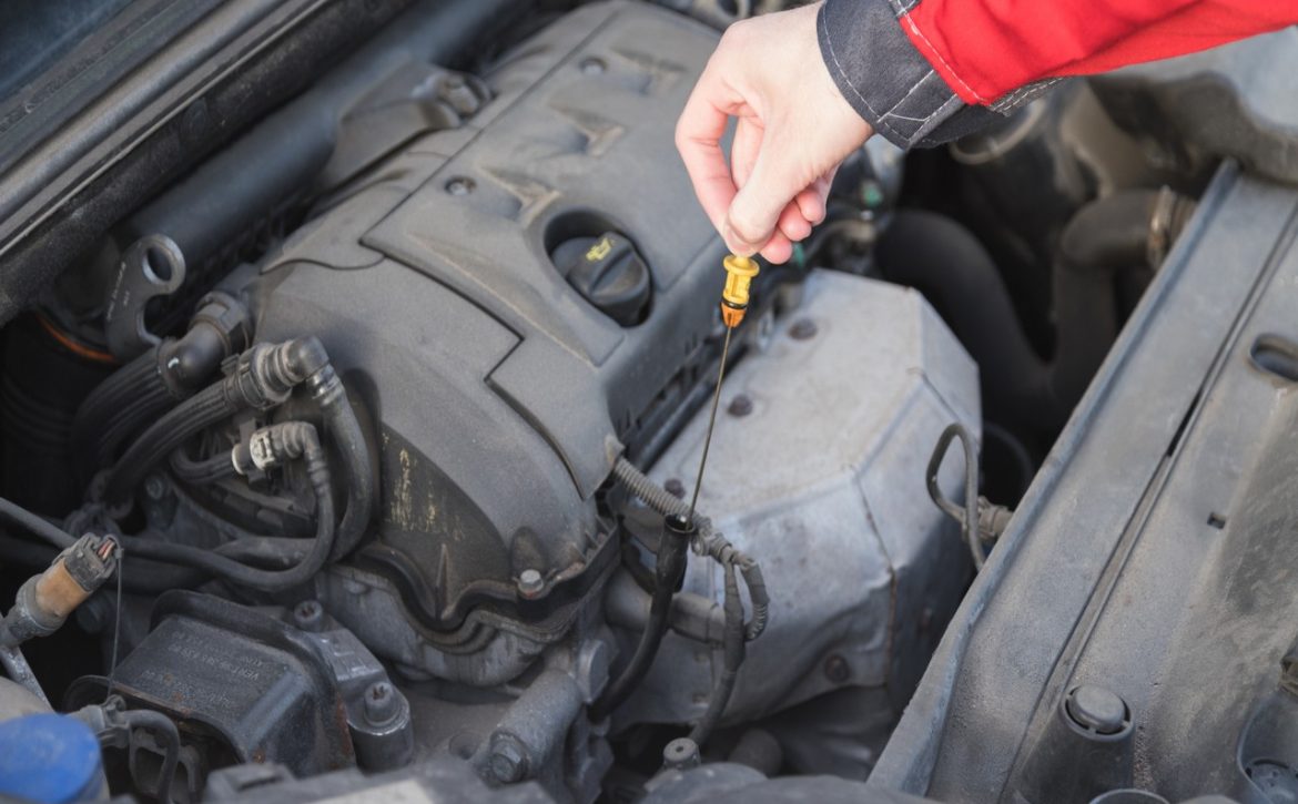Serviceman takes out a dipstick to check the oil level in the car engine.