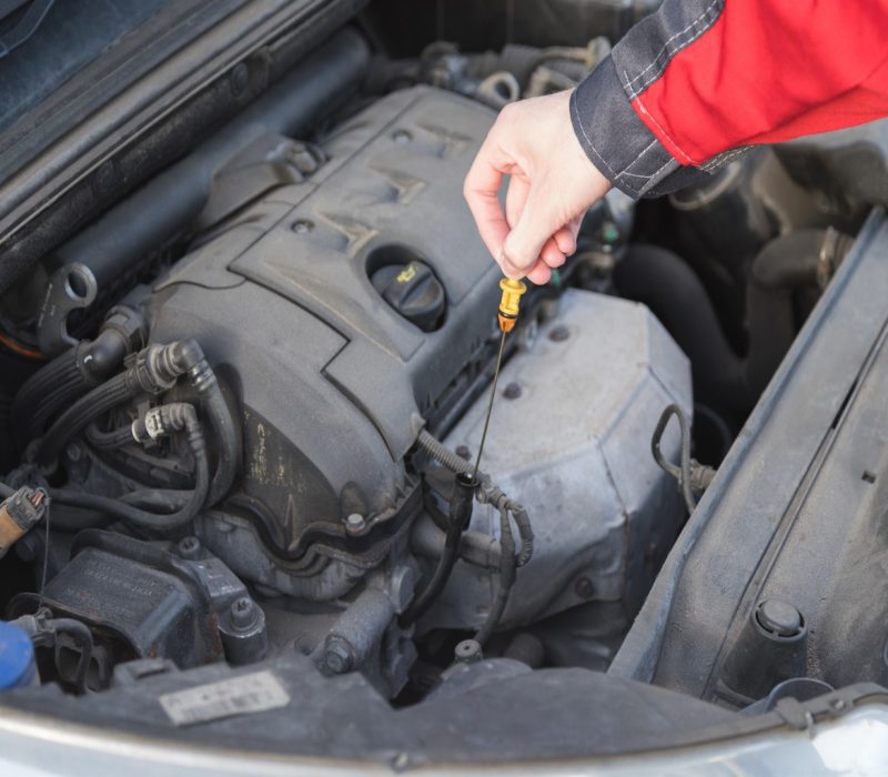 Serviceman takes out a dipstick to check the oil level in the car engine.